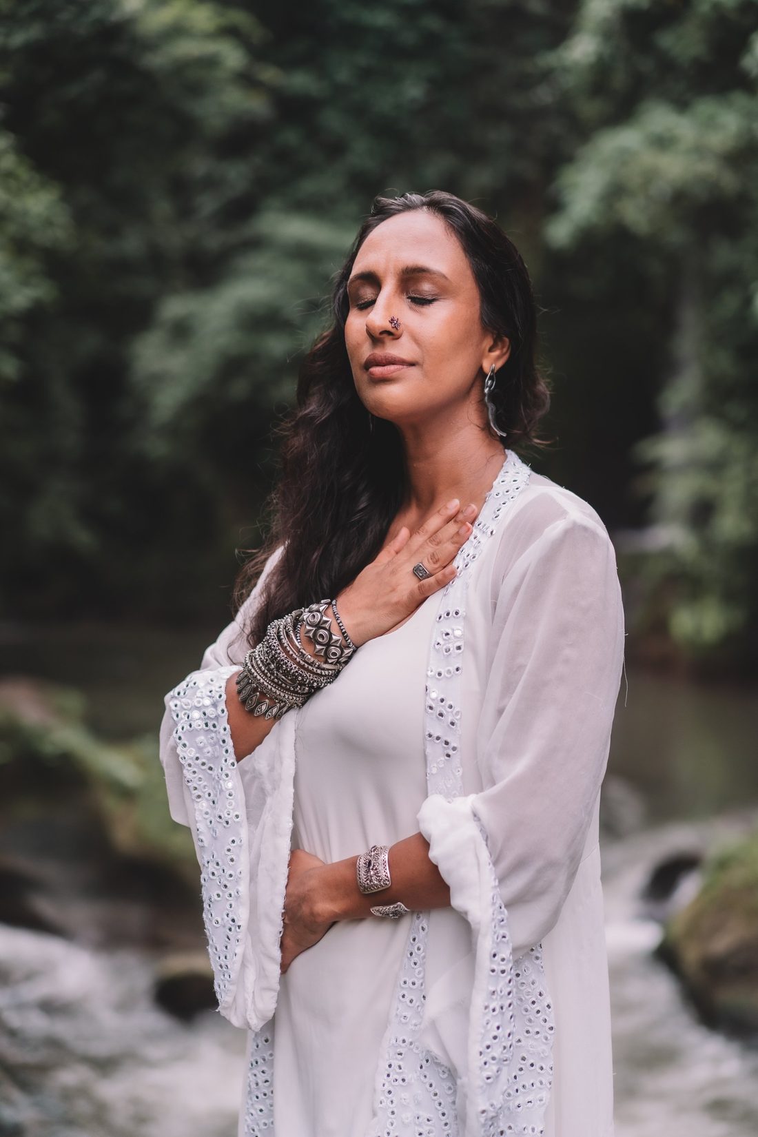 Sejal with eyes closed and a hand on her heart, standing by a river